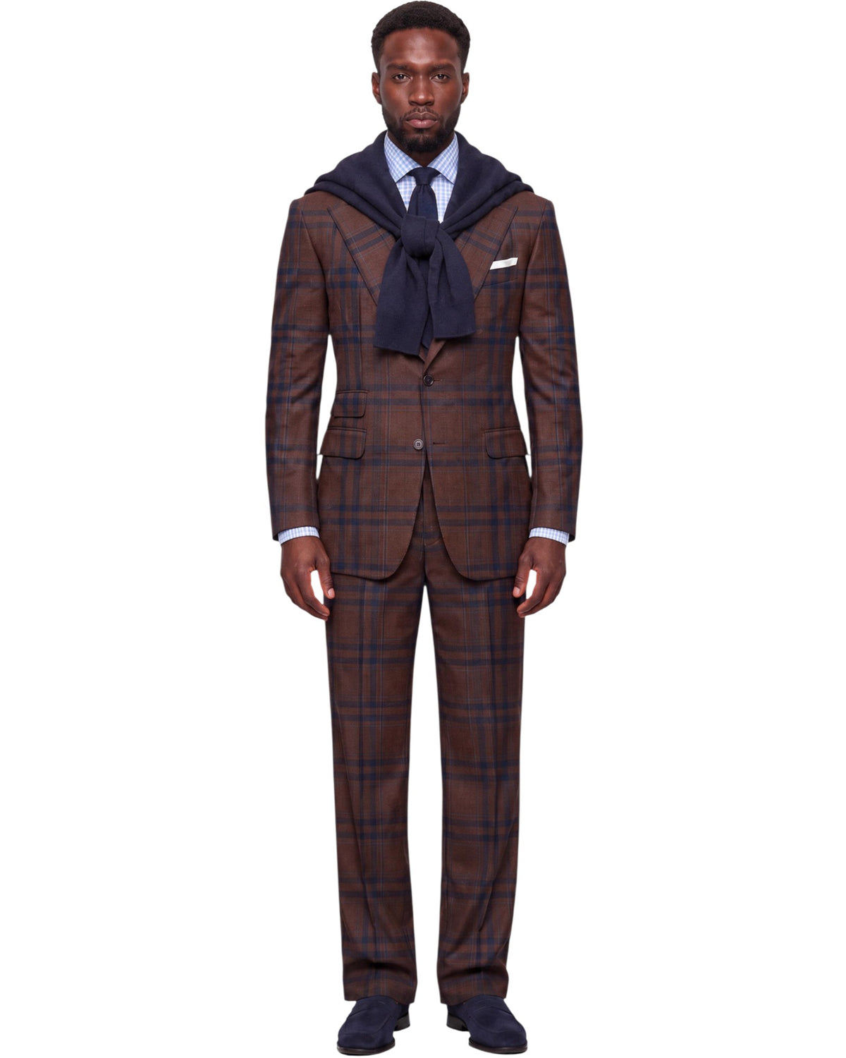 A man modeling a brown and navy plaid suit with a matching tie, dress shirt, and a navy hood draped over his shoulders, set against a plain white background.