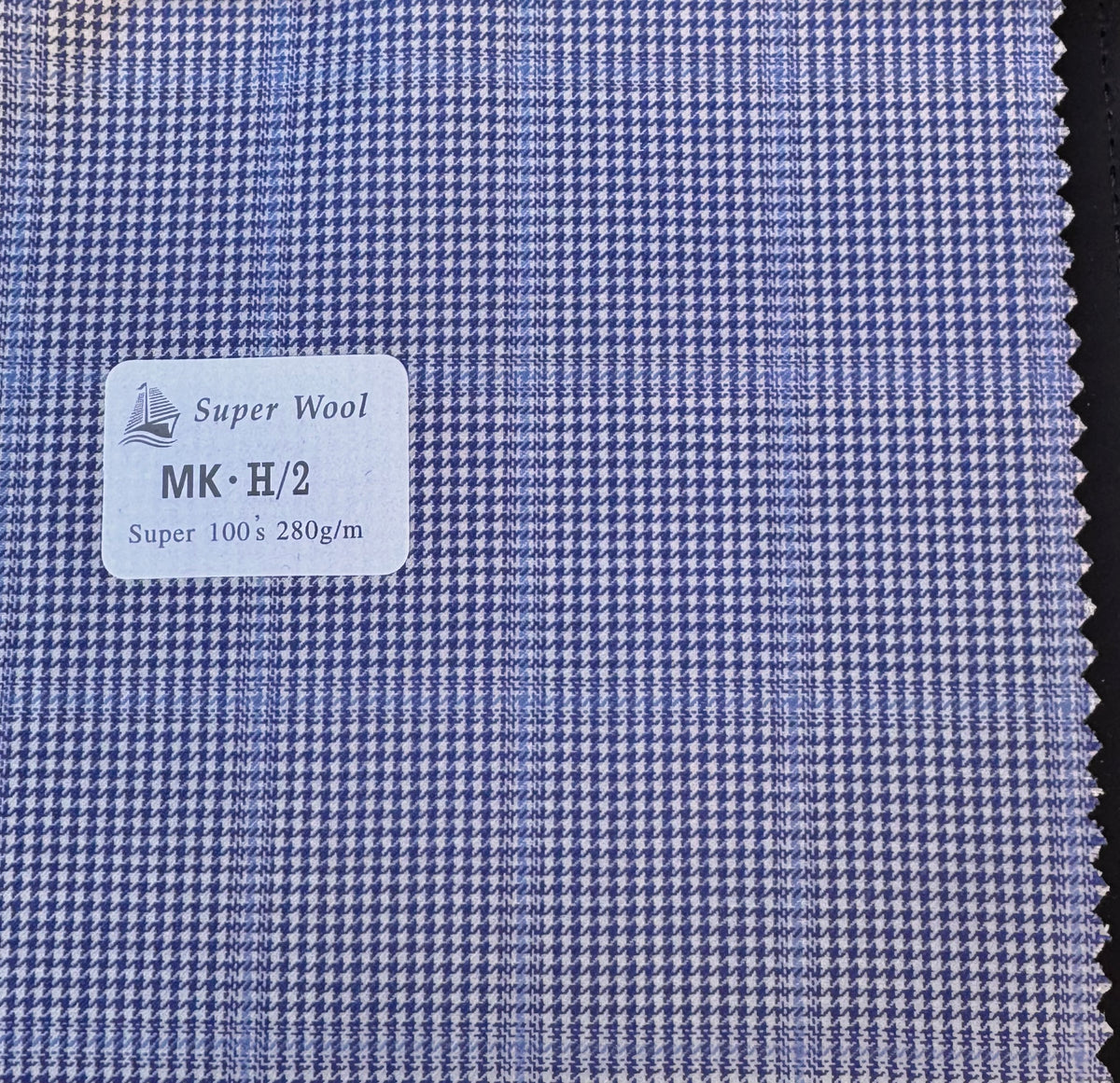 A close-up of a blue and white houndstooth wool fabric swatch with a white label reading 'Super Wool MK-H/2 Super 100% 280g/m'.