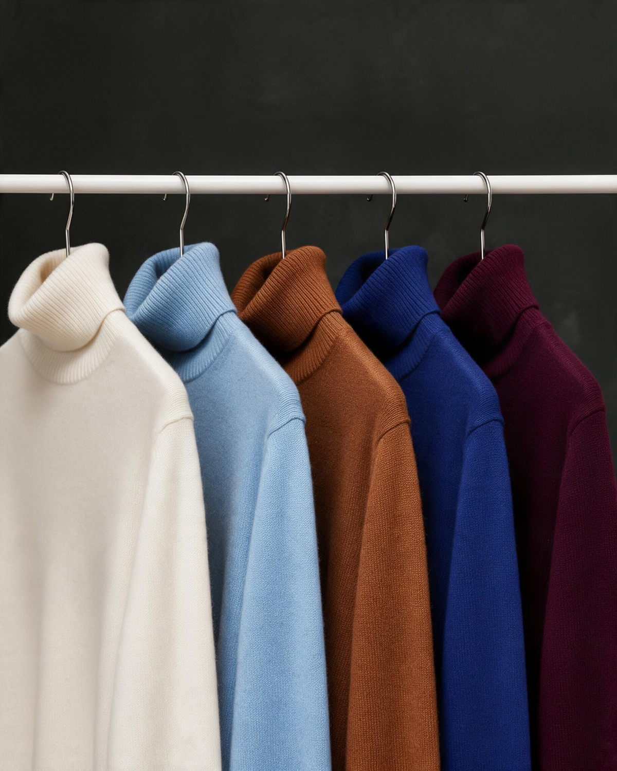 Terry Corbett New York cashmere turtlenecks in cream, light blue, cappuccino, navy, and burgundy on a clothing rack.
