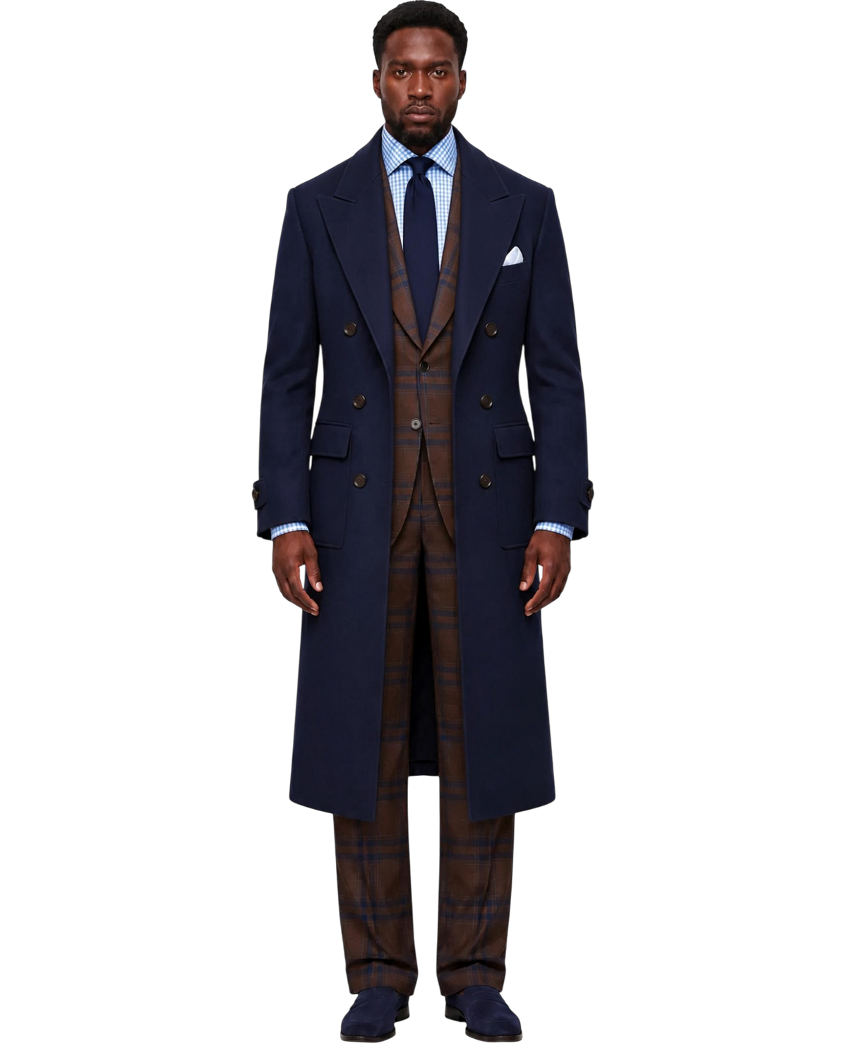 A man stands facing forward wearing a dark navy double-breasted overcoat over a brown plaid three-piece suit, a light blue dress shirt, a dark tie, and dark loafers, against a plain white background.