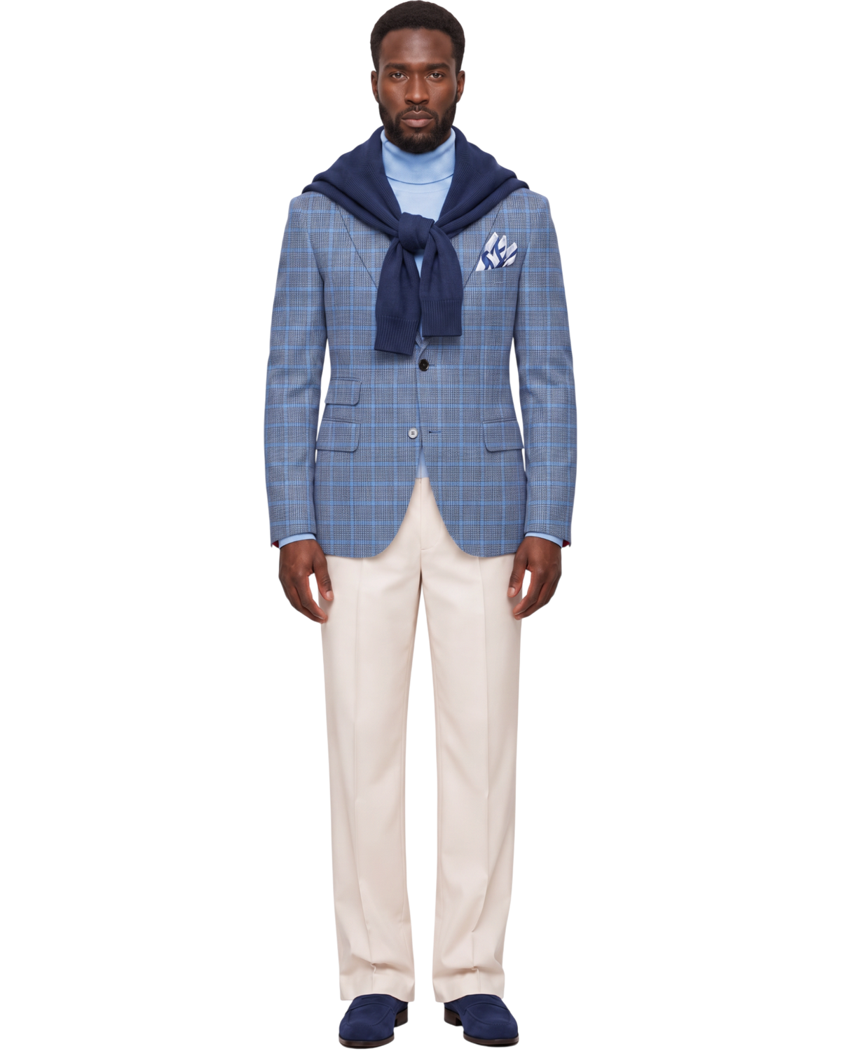 A full-length studio shot of a male model wearing a blue and white windowpane plaid blazer styled with a navy blue knit sweater draped over his shoulders, a light blue turtleneck, cream trousers, and navy loafers.